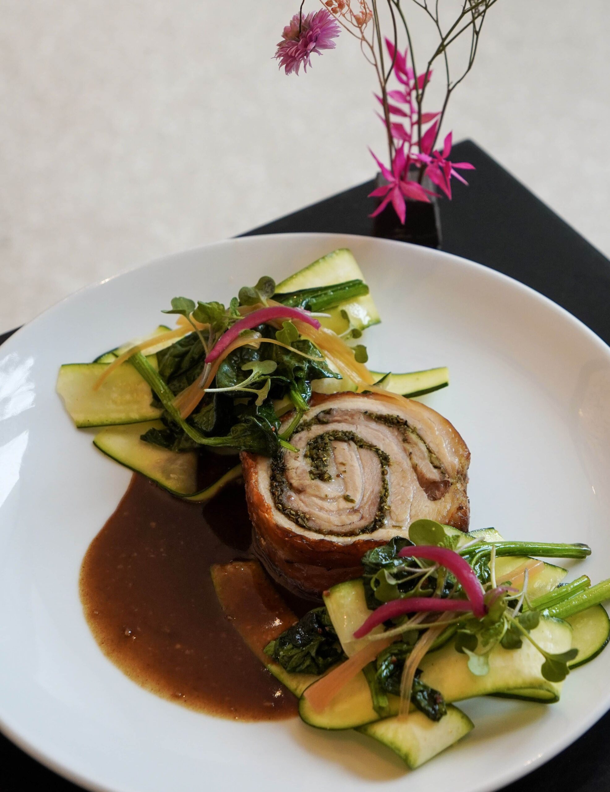 Porchetta aux herbes - Le Nabi Porchetta aux herbes, jus réduit, courgettes et tombée de légumes feuilles, sauce blanche à la ciboulette, pickles de rhubarbe, smash potatoes.